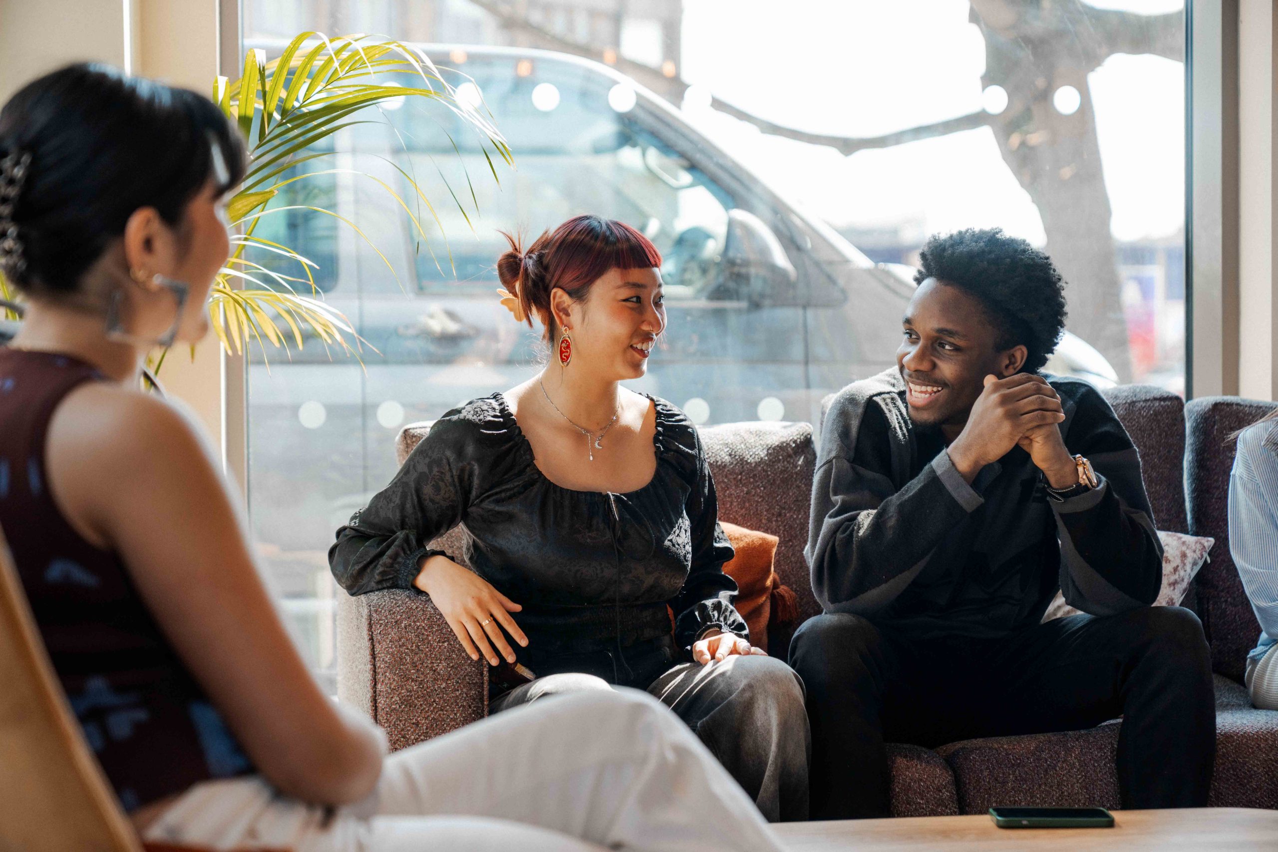 Three students chat in front of a glass window