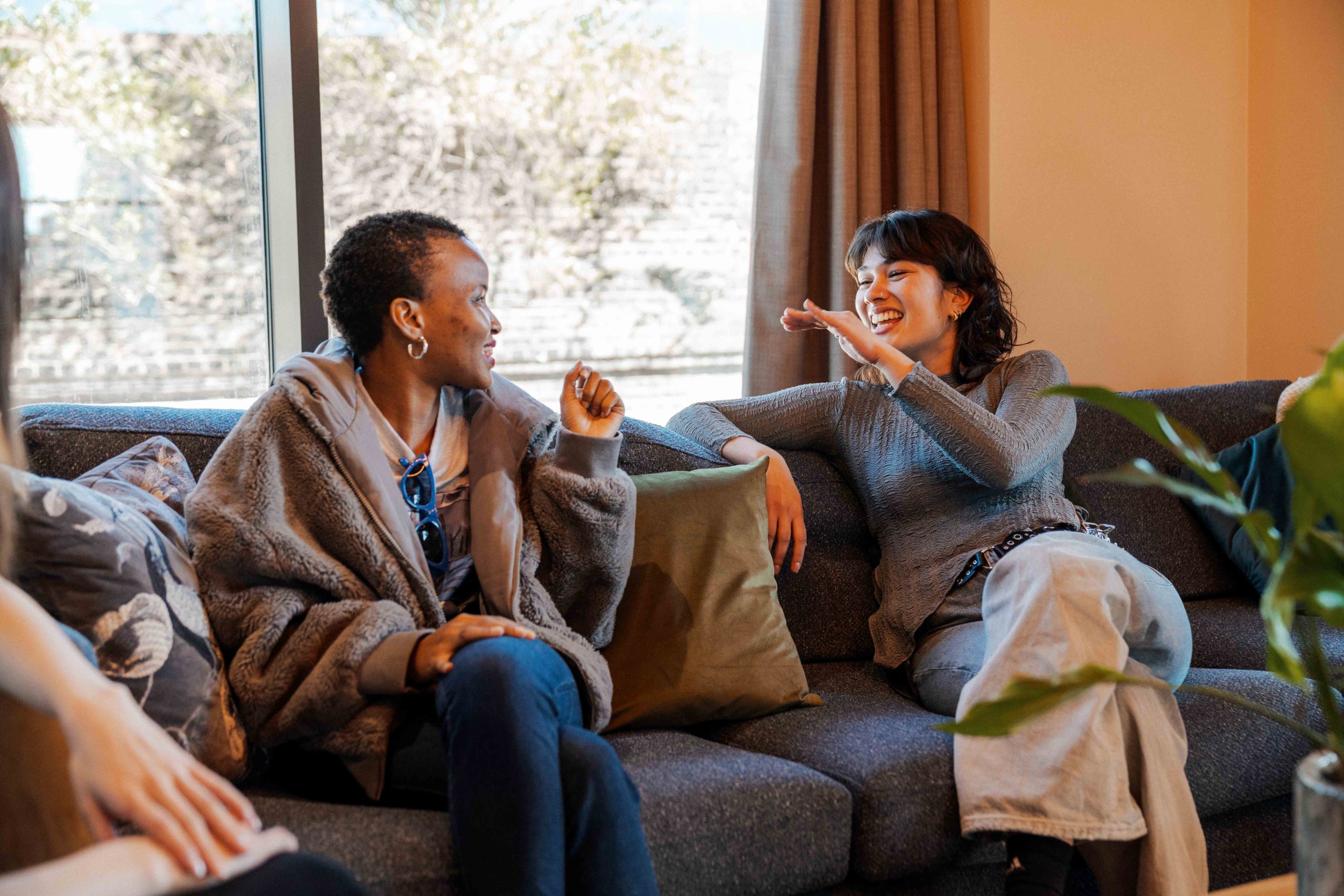 Two students chat and laugh on a sofa inside student accommodation