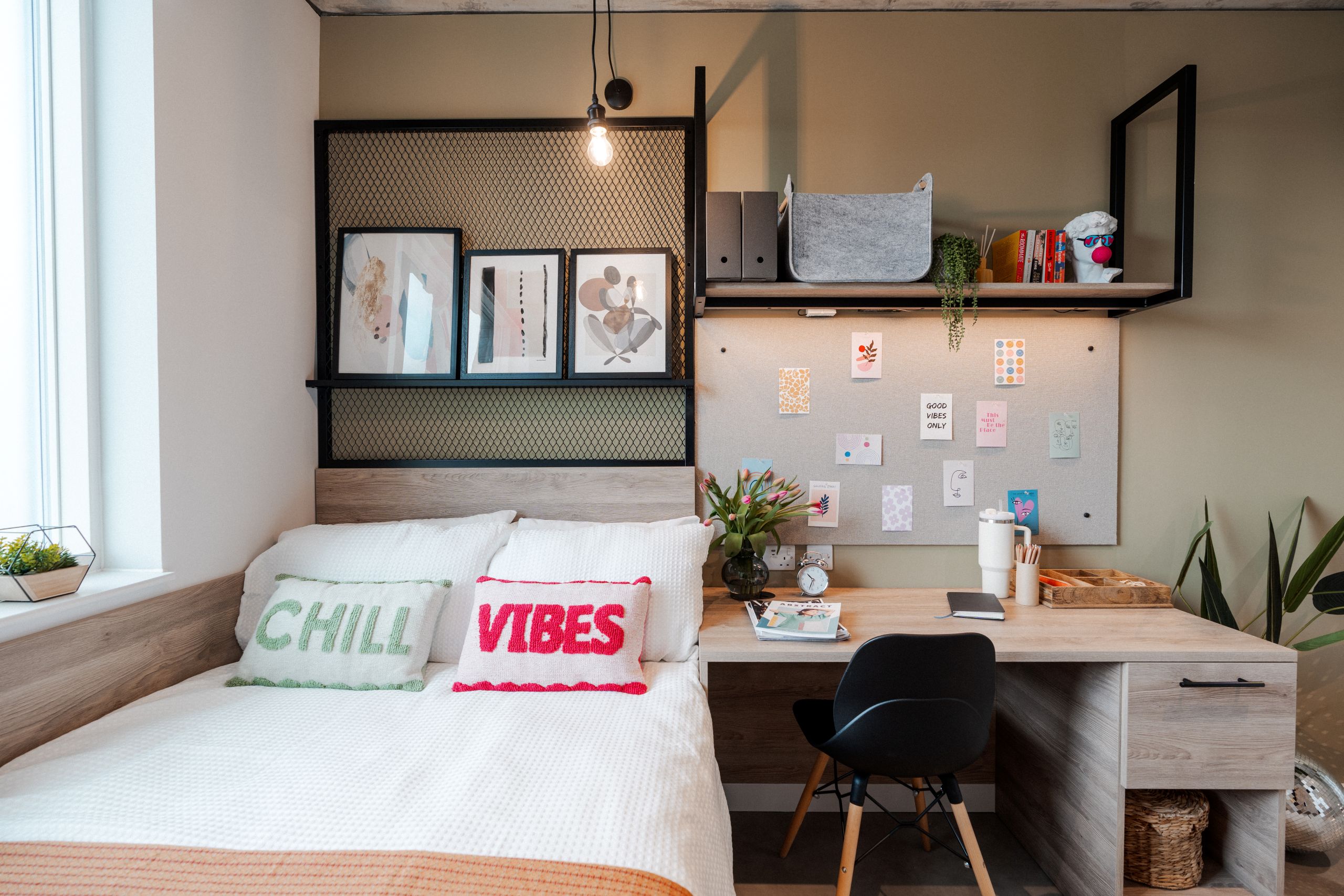 Student studio with desk, chair, and white double bed with cushions that read 'chill vibes'