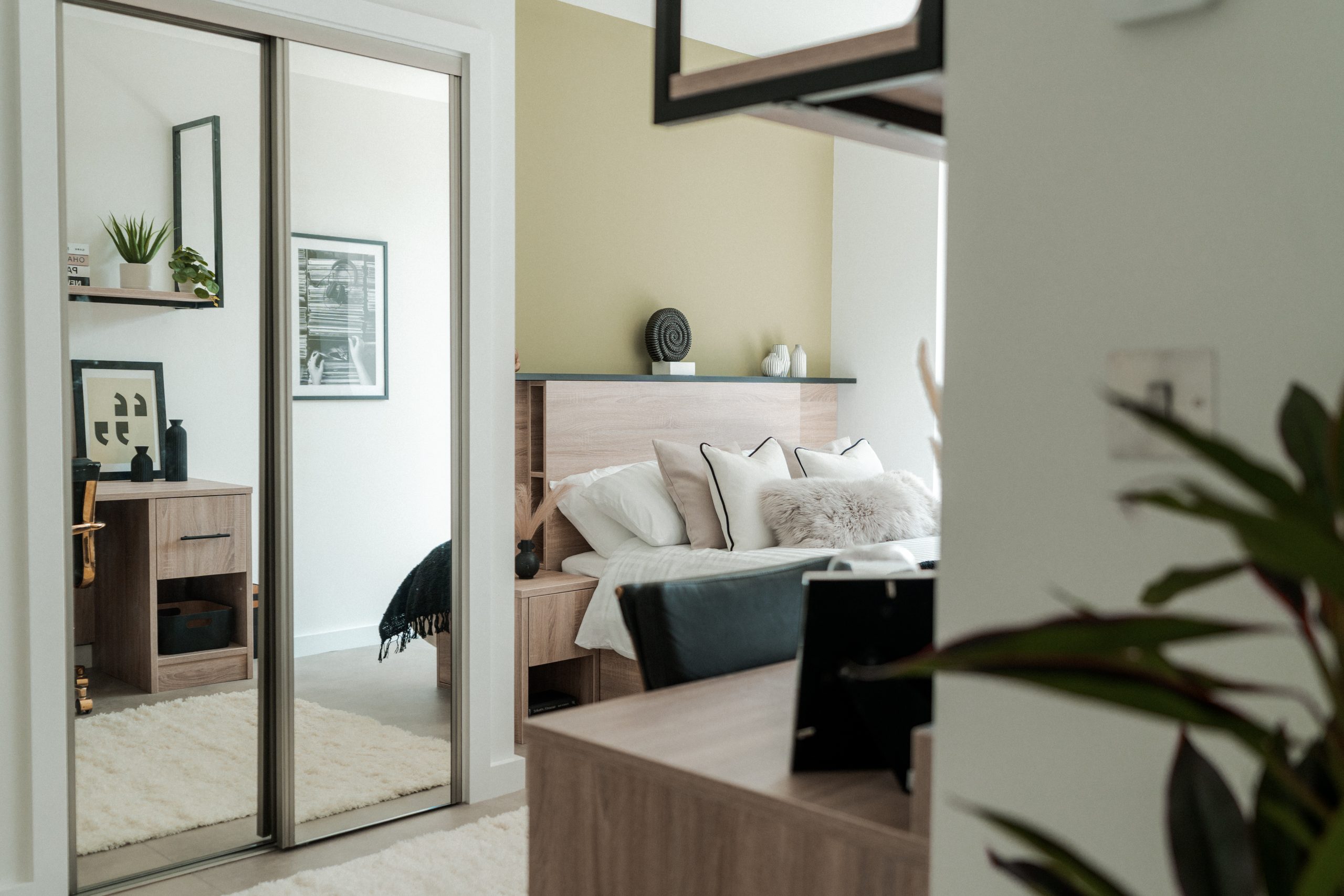 Mirrored wardrobes inside YourTRIBE's student accommodation reflect a wooden desk area, and there is a double bed in the background.