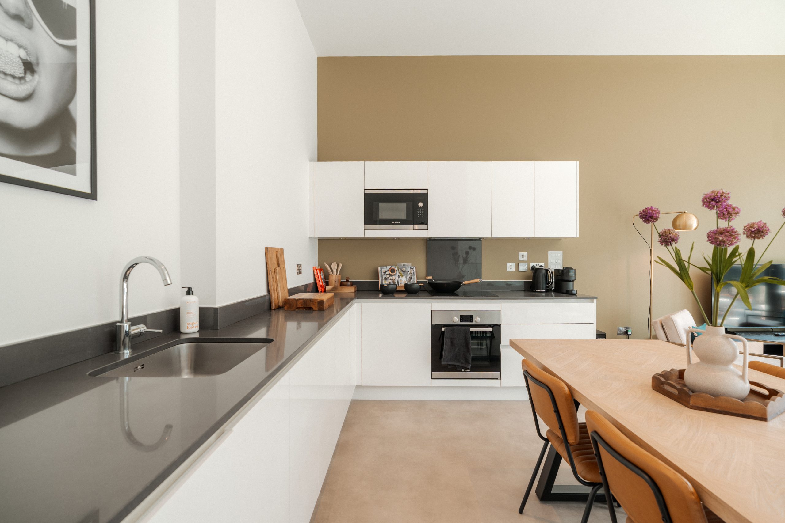 White shared kitchen inside YourTRIBE's Deptford student accommodation, with a wooden table and orange chairs.