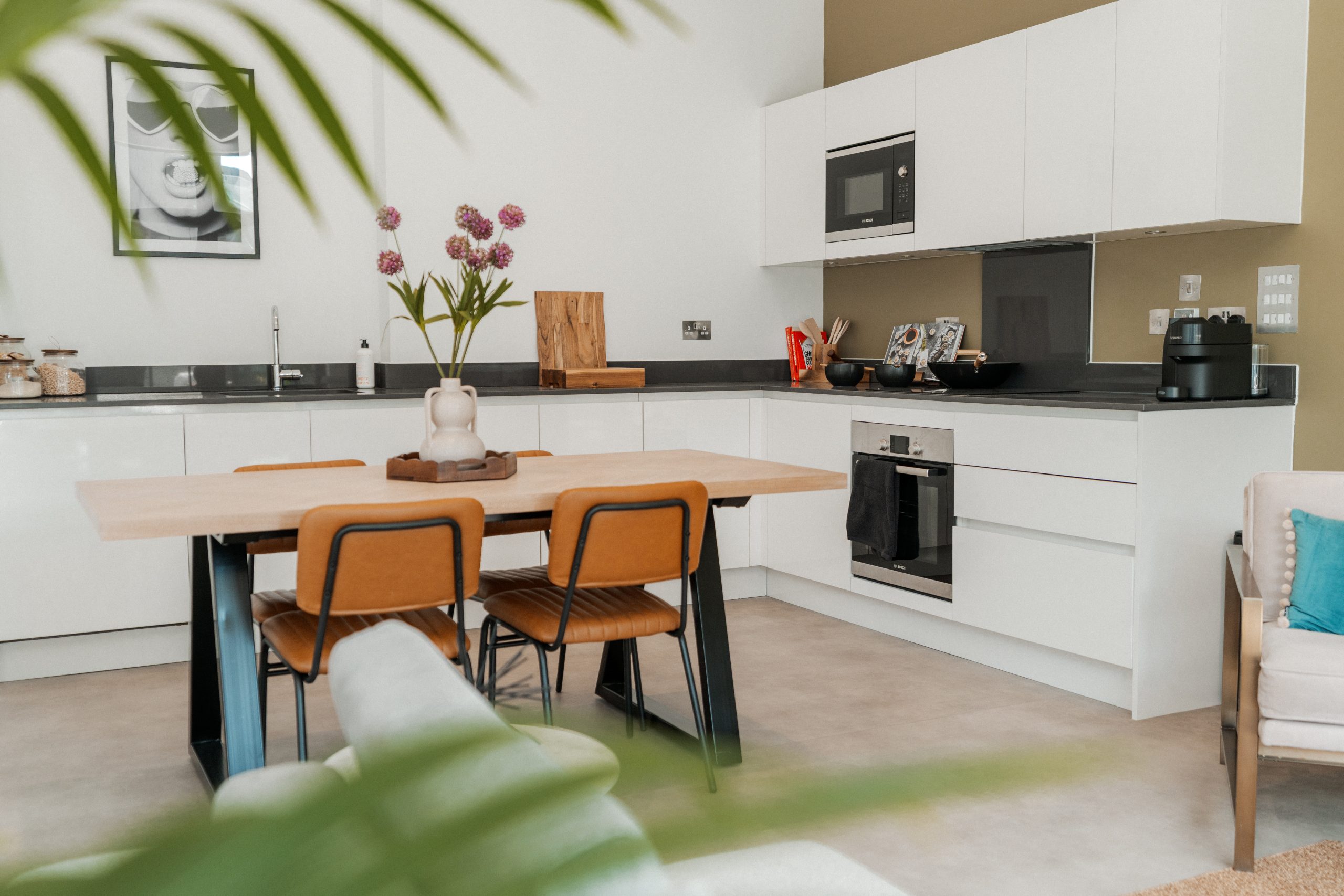 White kitchen area inside YourTRIBE's student accommodation with wooden table and orange chairs.