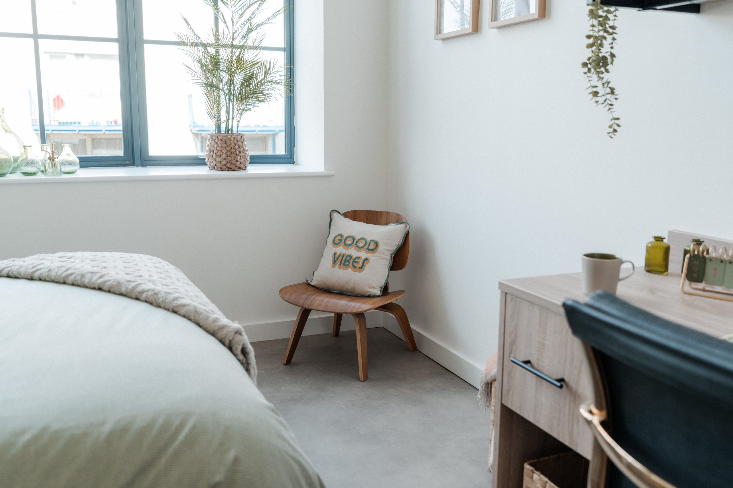 Corner of a student accommodation room. Wooden chair with a cushion that says 'good vibes, wooden desk and black leather chair.