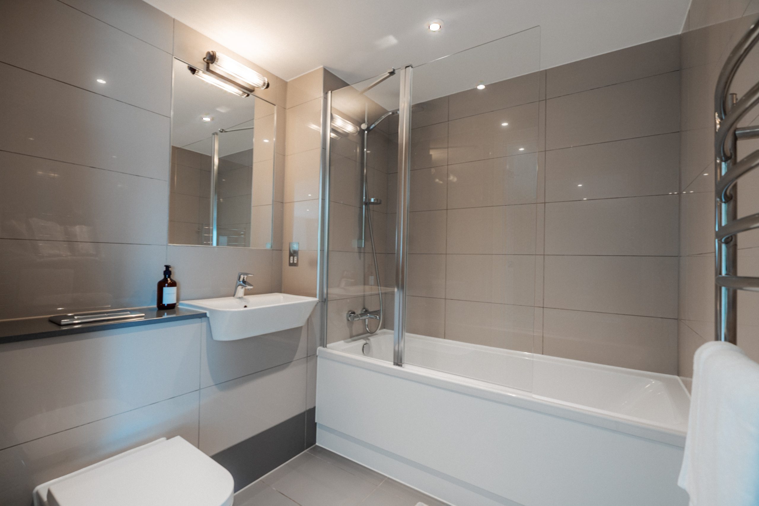 En-suite bathroom inside YourTRIBE's luxury student accommodation. White bath, toilet and sink with grey tiling.