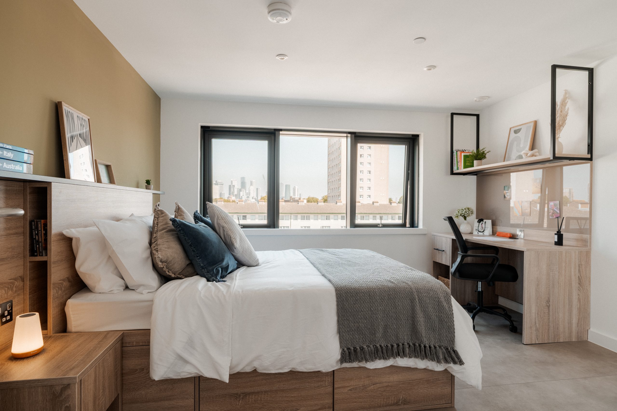 Premium room inside YourTRIBE's Deptford student accommodation, with a bed, desk, shelving and a bedside table.