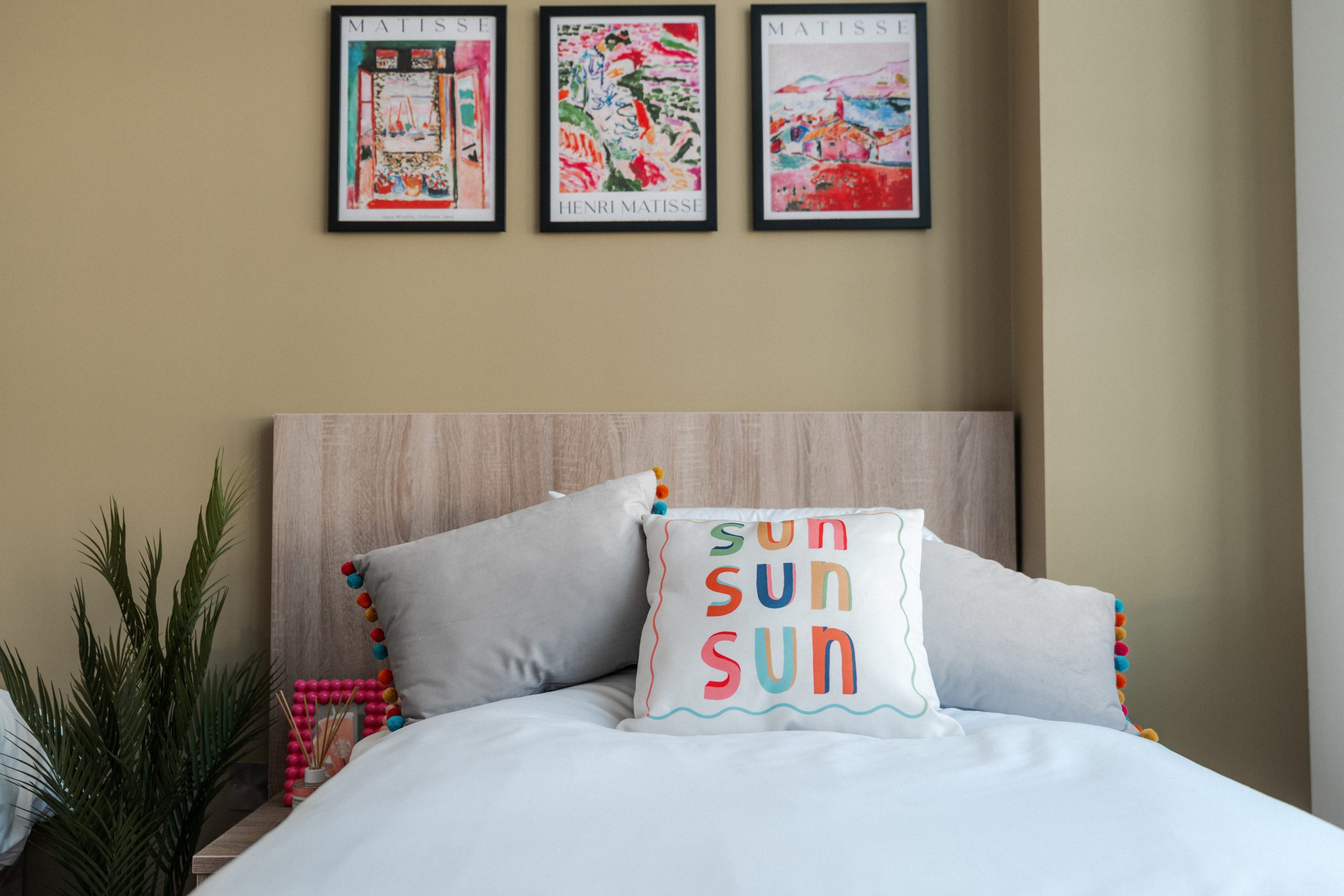 Bed inside YourTRIBE's student accommodation with white bedding and cushions that read 'sun, sun, sun'. Matisse artwork is above the bed.