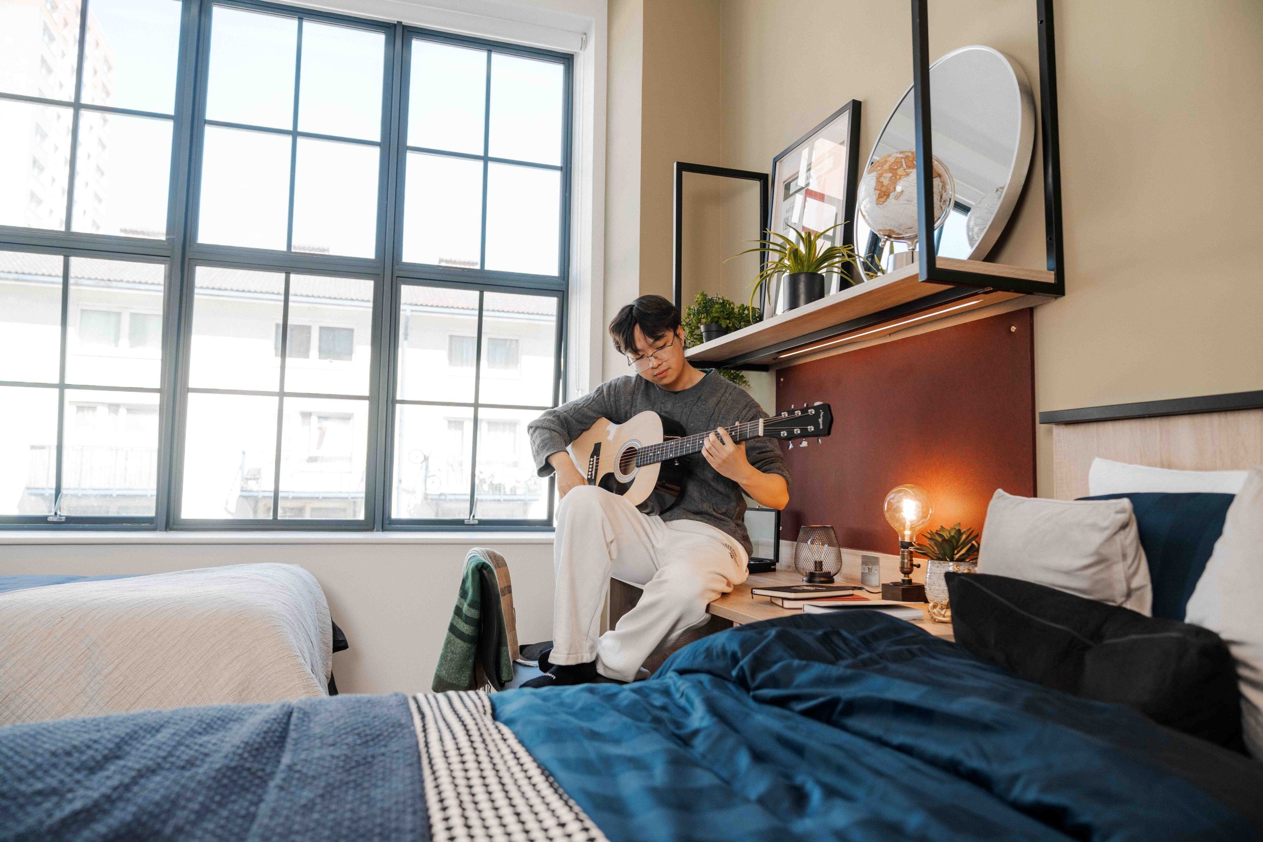 Student playing guitar in the corner of his bedroom