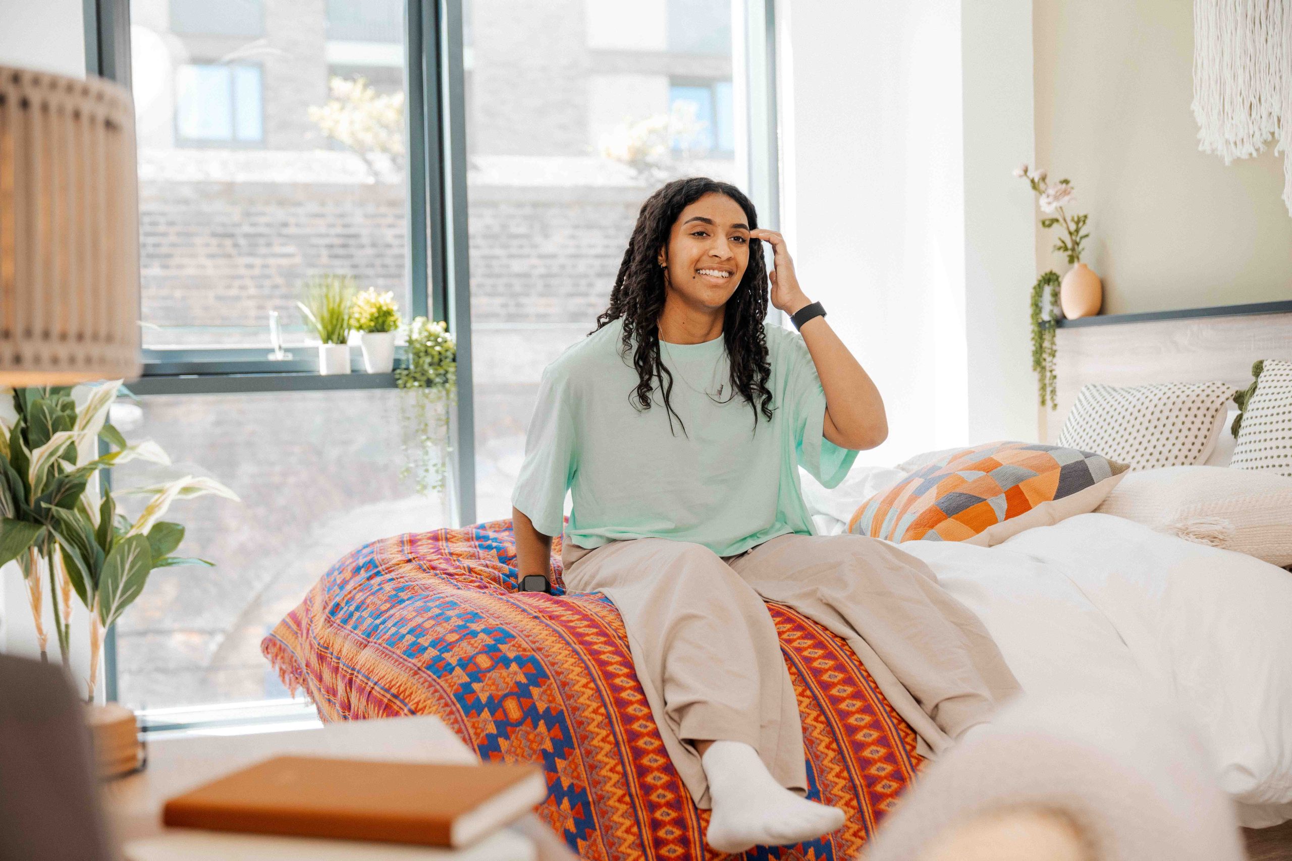 Student sits on her bed smiling, pushing her hair back
