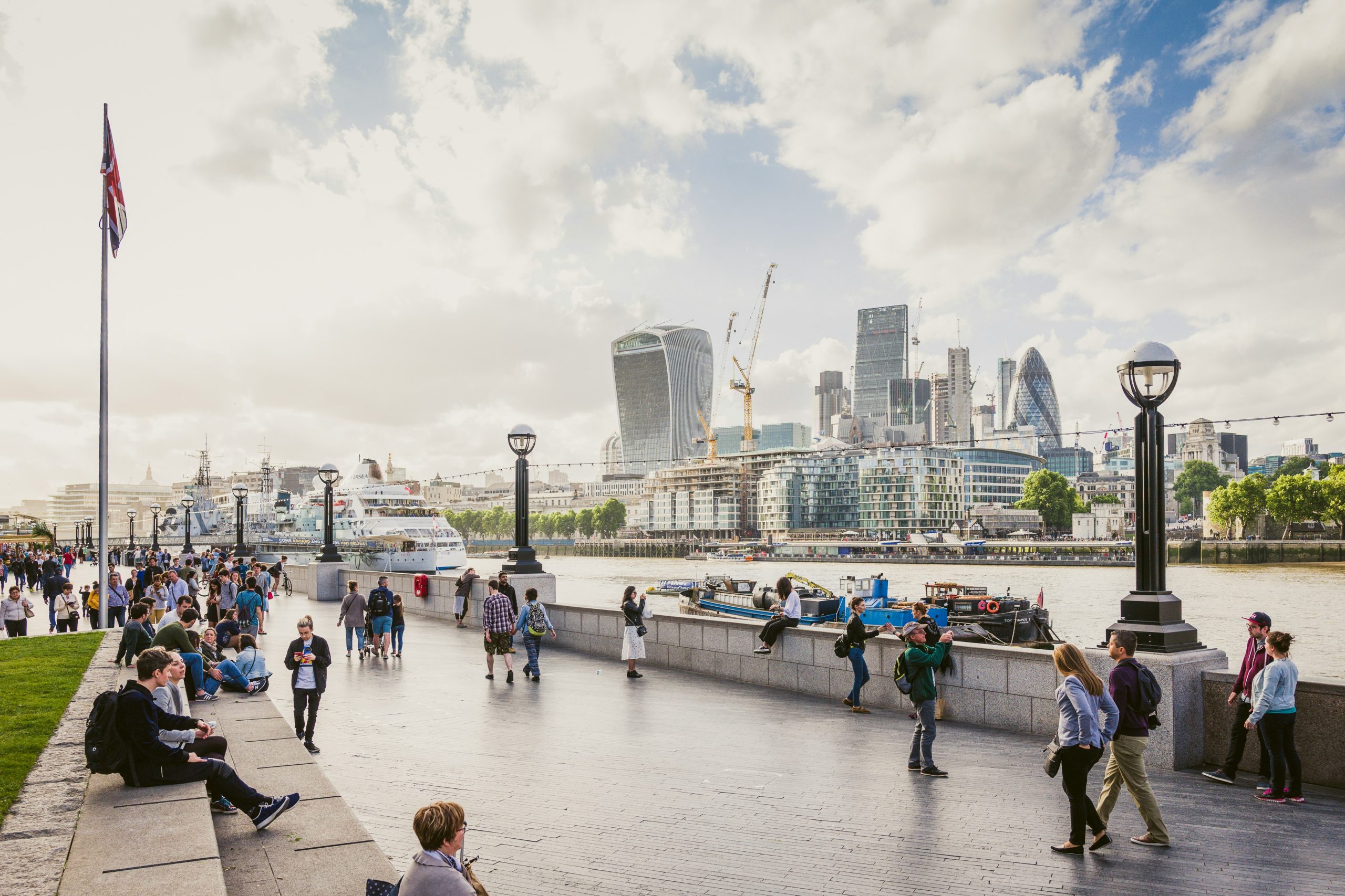 People walking beside the River Thames with the City of London skyline across the water