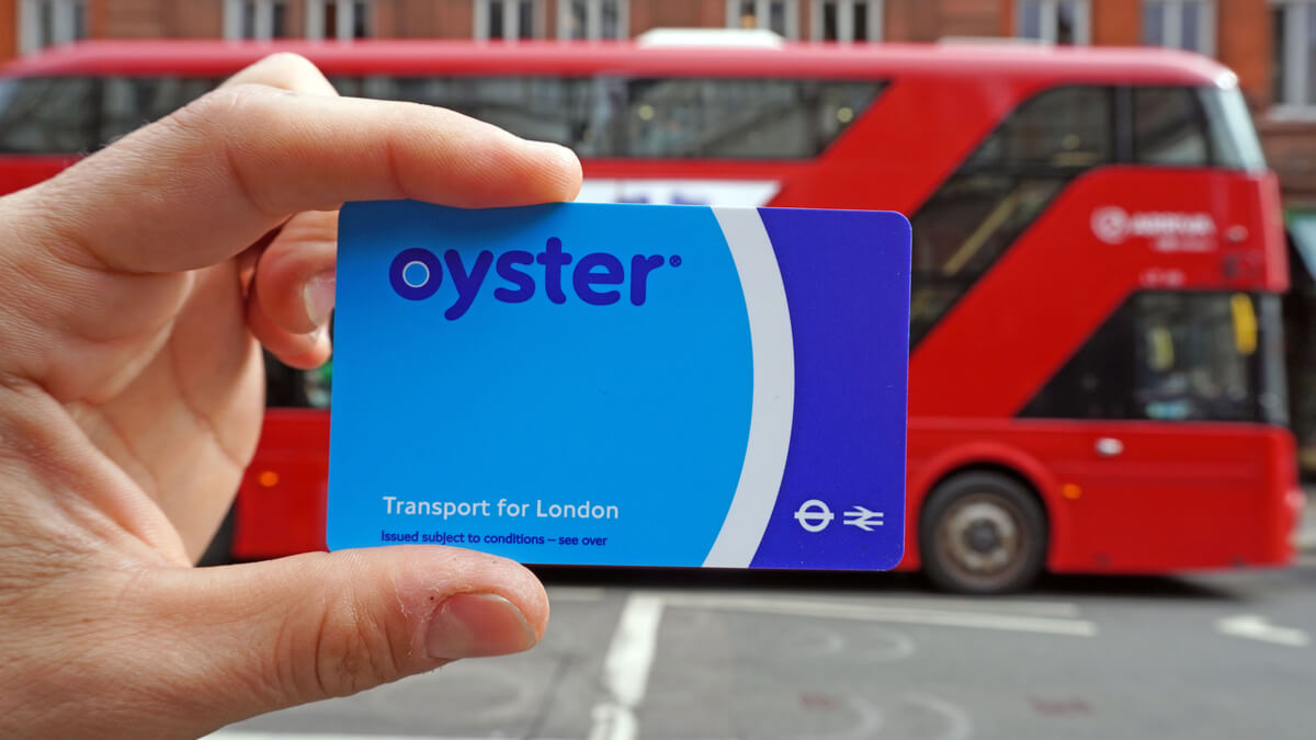 Hand holding a blue Oyster card in front of a red London bus